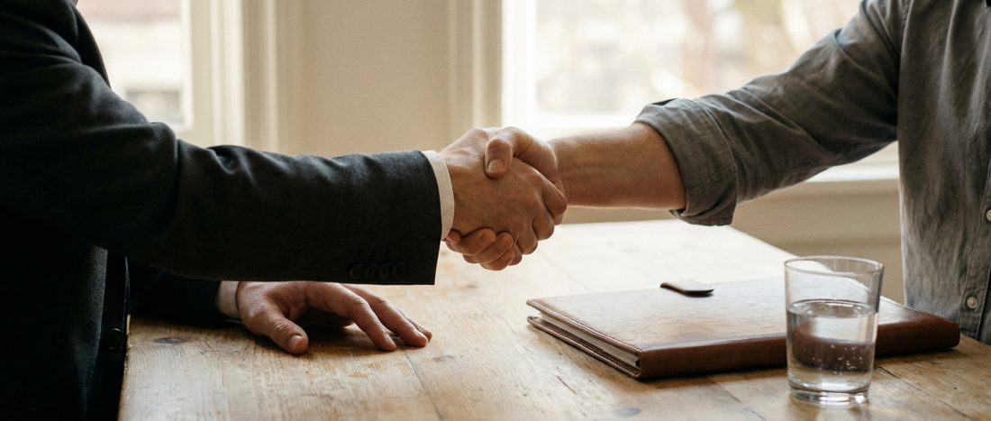 Two people shaking hands across a table at the end of a meeting